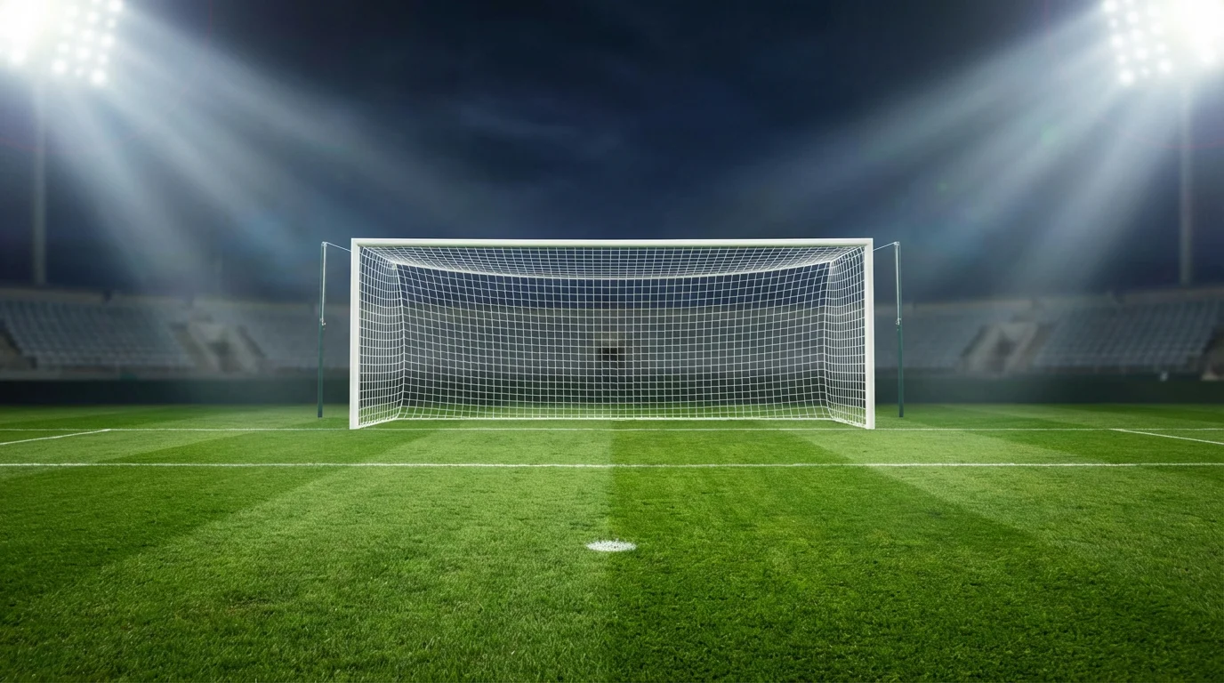Portería de fútbol vista desde el área de penalti en un campo de césped natural iluminado por focos